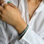 Close-up of a person wearing a white shirt with a blue beaded bracelet on a blurred background