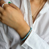 Close-up of a person wearing a white shirt with a blue beaded bracelet on a blurred background