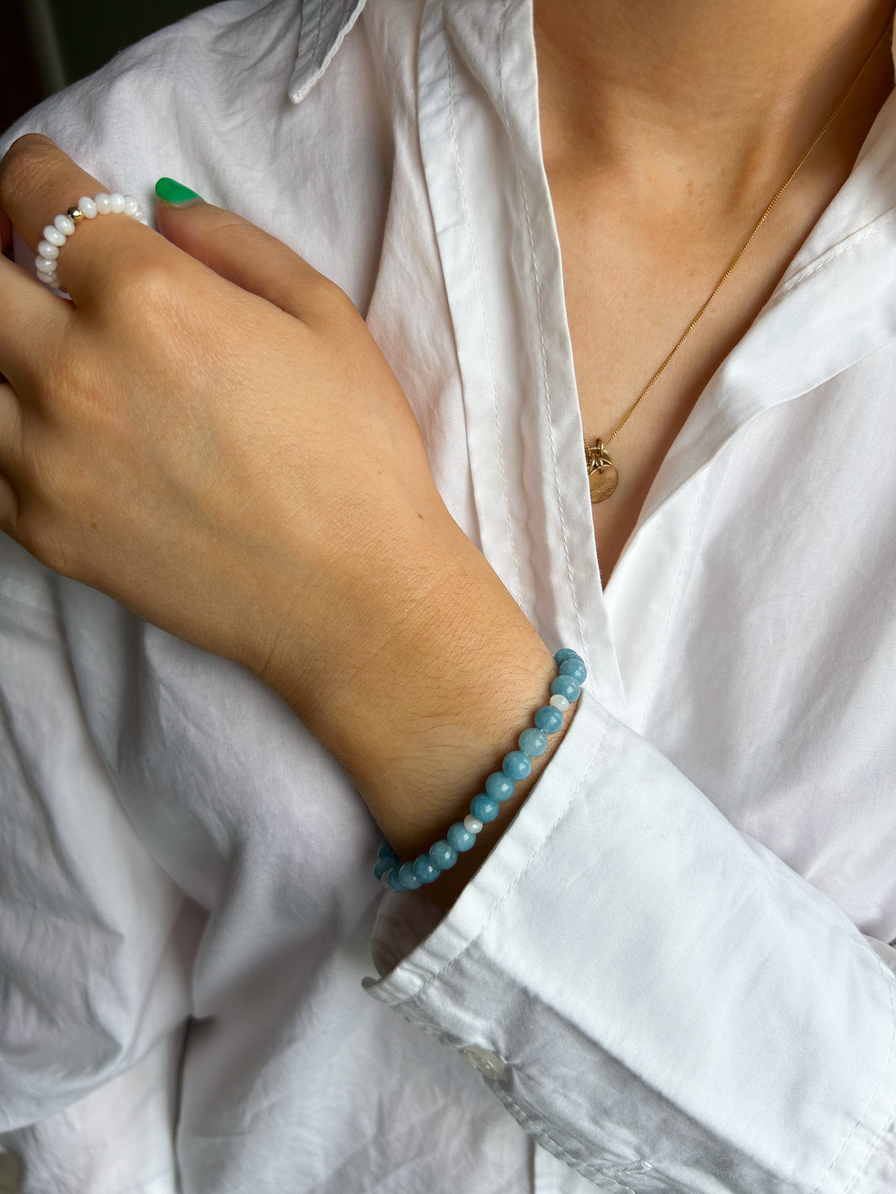 Close-up of a person wearing a white shirt with a blue beaded bracelet on a blurred background