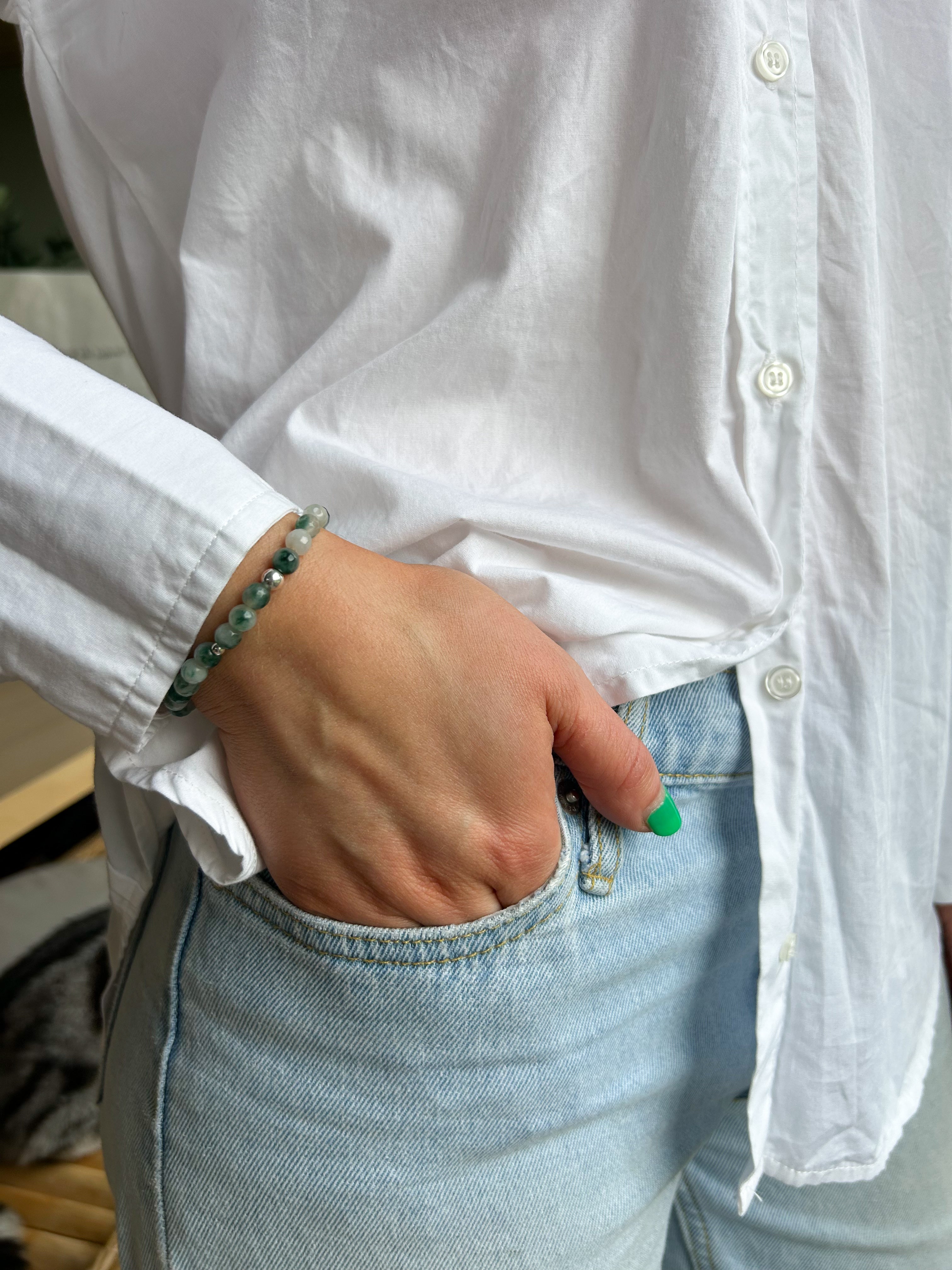 Person wearing a white shirt and light blue jeans with a bracelet on a blurred background