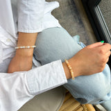 Person wearing a white shirt and light blue jeans with a bracelet on a wooden chair.