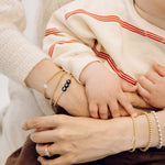 Little boy holding his mum's hands. She is wearing a stack of gold, personalised bracelets by ivy & gold 