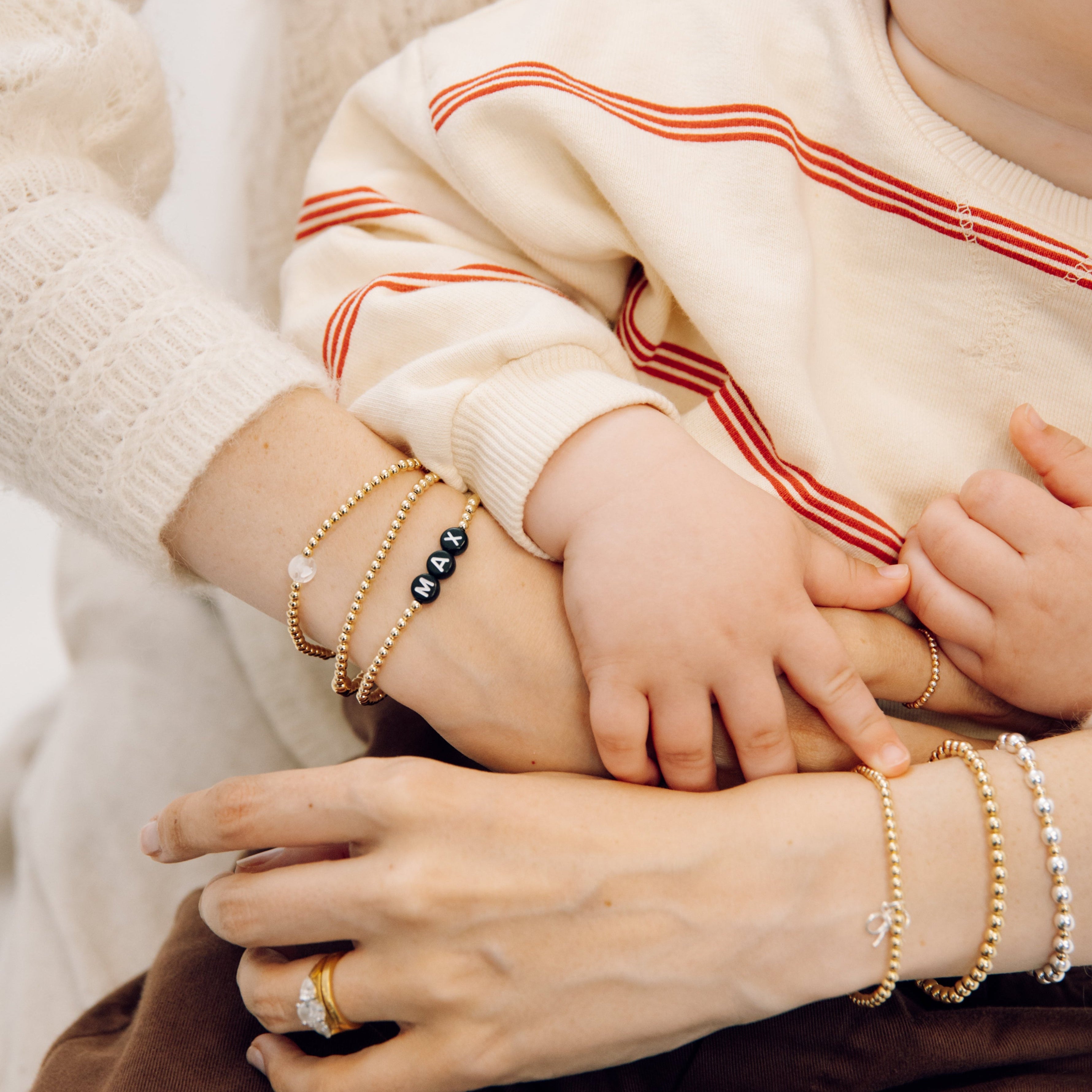 Little boy holding his mum's hands. She is wearing a stack of gold, personalised bracelets by ivy & gold 